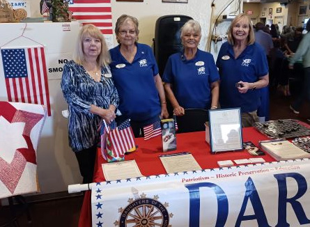 Photograph of four women standing behind a table; a banner reads DAR, Daughters of the American Revolution; photo taken by a chapter member and used with permission